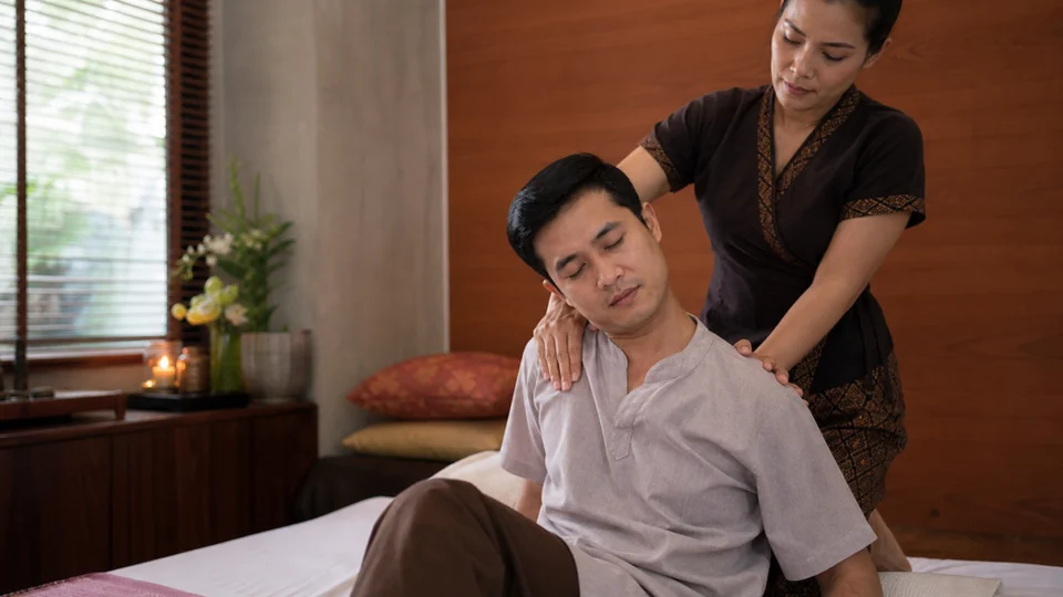 Professionelle Thai-Massage für die Schulter in einem ruhigen Spa-Raum mit einem vollständig bekleideten männlichen Kunden